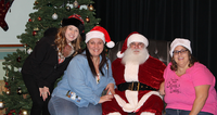 Three women posing with Santa Claus next to a Christmas tree.